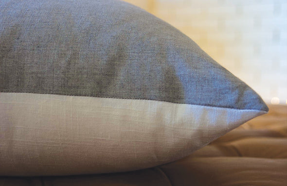 Close up of large pillow lying horizontally showing the fine seem work and texture of the blue-gray linen side and white linen side.